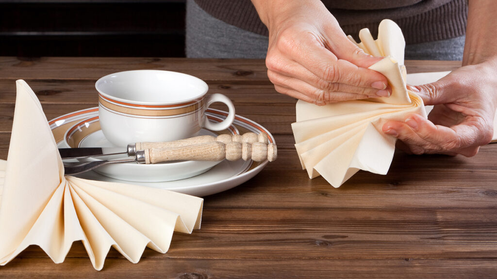 overhead shot of a person's hands folding a napkin for a dinner place setting
