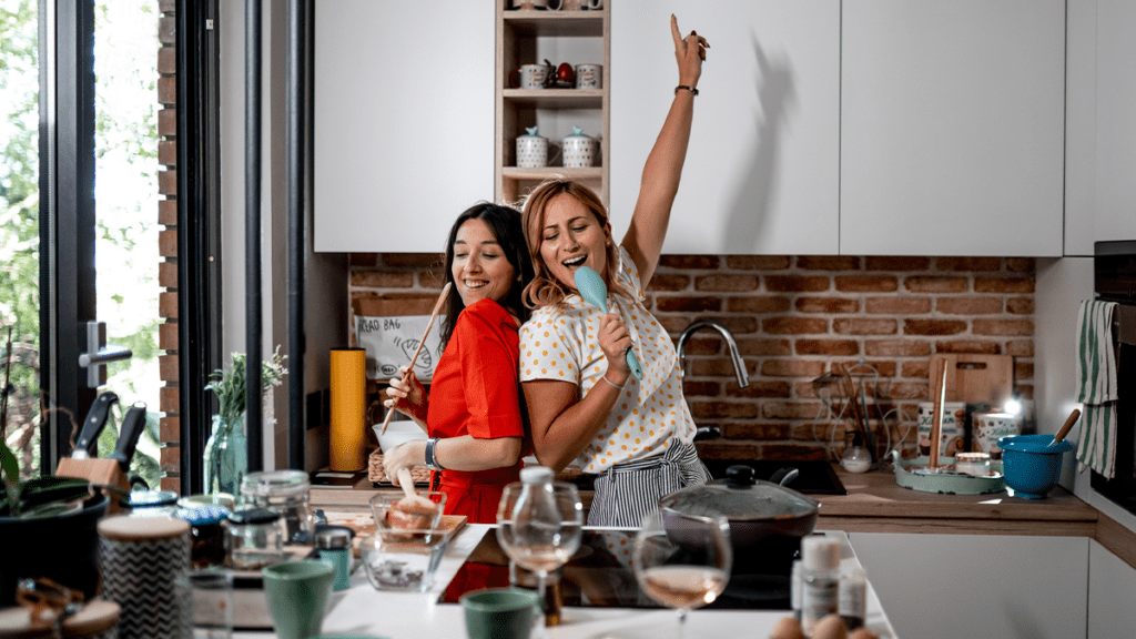 two women in the kitchen, using cooking utensils as microphones and percusive instruments