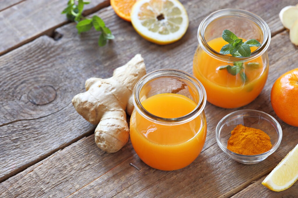 A glass of orange juice accompanied by ginger and powdered turmeric