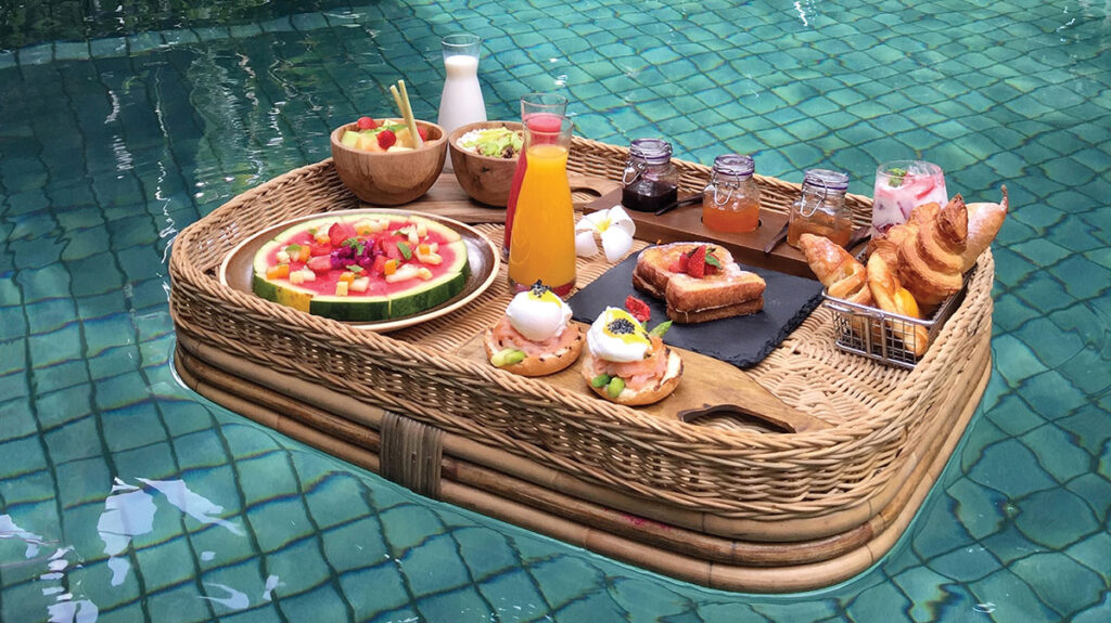 A photo of a full breakfast tray, including orange juice, toast, and other appetizers, floating in a pool