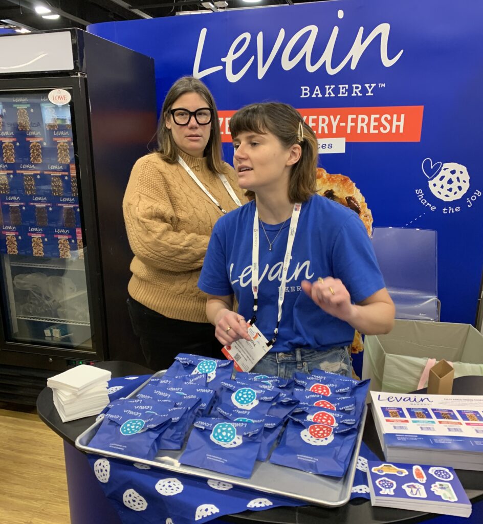 A representative hands out cookies and information from the Levain Bakery booth at Expo West 2022