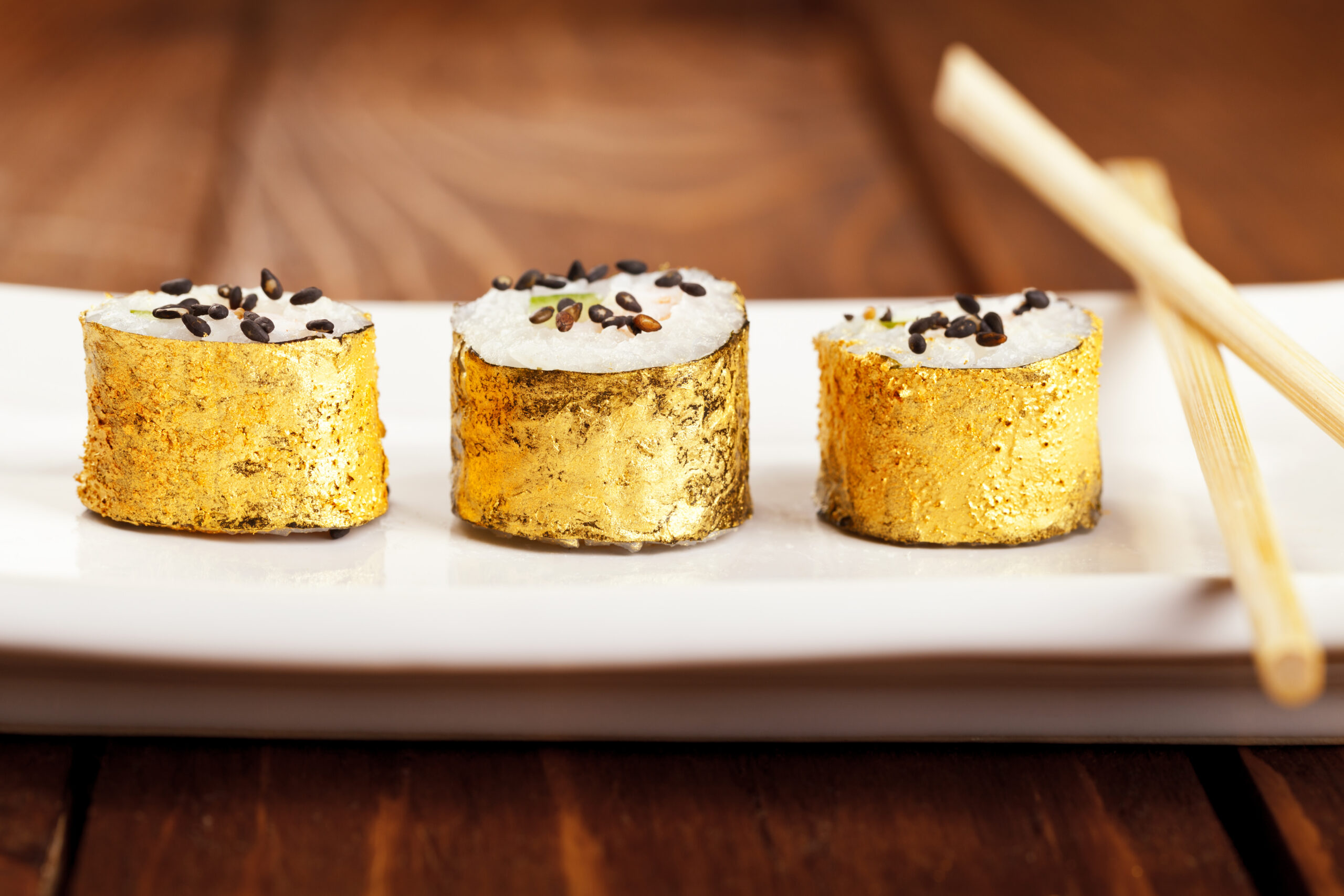 Three pieces of sushi wrapped with gold seaweed lined up on a plate.